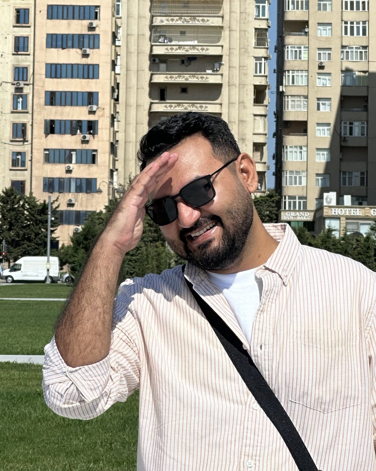 Ahmed Shakeel in sunglasses, shading his eyes, with tall apartment buildings and blue sky behind him